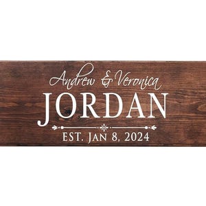 Puede incluir: Un letrero rectangular de madera marr&oacute;n oscuro con los nombres "Andrew & Veronica JORDAN" en blanco. Debajo, el texto "EST. JAN 8, 2024" tambi&eacute;n en blanco. La madera est&aacute; te&ntilde;ida.