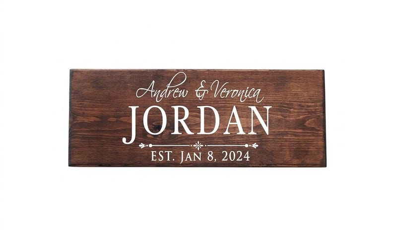 Puede incluir: Un letrero rectangular de madera marr&oacute;n oscuro con los nombres "Andrew & Veronica JORDAN" en blanco. Debajo, el texto "EST. JAN 8, 2024" tambi&eacute;n en blanco. La madera est&aacute; te&ntilde;ida.
