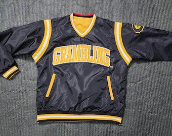 May include: Black and yellow Grambling State University pullover jacket. The jacket has a V-neck collar with a yellow interior and a red trim. The word "GRAMBLING" is across the chest in yellow block letters.