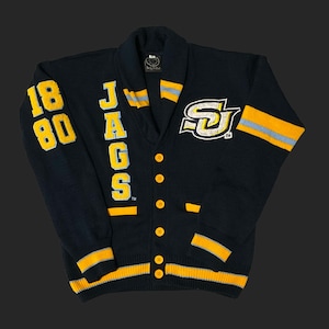 May include: A navy blue cardigan sweater with yellow and white accents. The sweater features the word "JAGS" vertically down the front, the numbers "1880" on the left sleeve, and a logo on the right chest. Yellow and white stripes adorn the cuffs and collar.