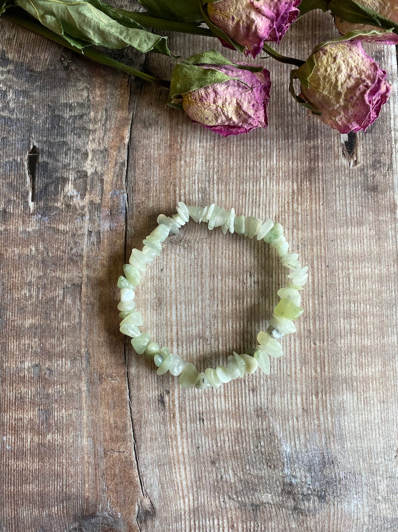 May include: A green jade chip bracelet made of small, irregular shaped stones. The bracelet is on a wooden surface.