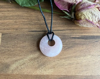 May include: A pink rose quartz donut pendant on a black cord necklace. The pendant is smooth and polished.