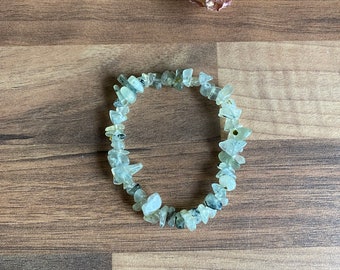 May include: A bracelet made of light green and clear gemstone chips. The bracelet is made of natural stones and is strung on a clear elastic cord.