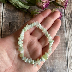 May include: A green jade chip bracelet with a light green color. The bracelet is made of small, irregular shaped chips of jade.