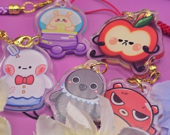 May include: A collection of colorful acrylic charms featuring cartoon characters. The charms include a snowman, an alien in a spaceship, a penguin, an apple, and a red creature. Each charm has a gold-colored clasp and a decorative cord.