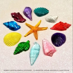 May include: Twelve assorted sugar seashells and a starfish cake topper. The seashells are in various colors, including red, blue, green, yellow, purple, and pink. The starfish is orange.