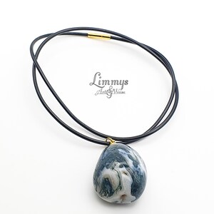 Puede incluir: Un collar de cuero negro con un colgante ovalado grande. El colgante es una mezcla de colores azul, blanco y verde. El collar tiene un cierre dorado. El texto "Limmys Art & Weise" est&aacute; en la imagen.