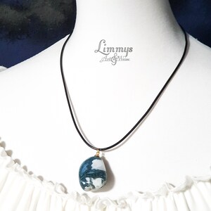 Puede incluir: Un collar con colgante de piedra azul, blanca y verde. La piedra cuelga de un cord&oacute;n negro con una fianza dorada. El collar se exhibe en un maniqu&iacute; blanco. La marca "Limmys Art & Weise" es visible.