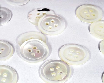 May include: A collection of white mother of pearl buttons with four holes each. The buttons are arranged in a random pattern on a white surface.