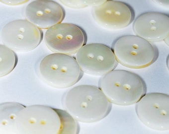 May include: A collection of white mother of pearl buttons with two holes each. The buttons are round and have a smooth, glossy finish.