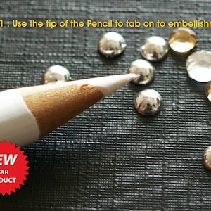 Puede incluir: Un lápiz blanco con una base de madera marrón se utiliza para presionar sobre adornos plateados y dorados. El texto "NEW STAR PRODUCT" está en una forma de estrella roja.