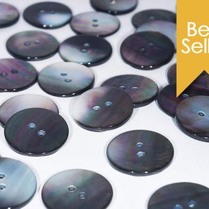 May include: A collection of 20 black and iridescent mother of pearl buttons with two holes each. The buttons are round and have a smooth, polished finish.