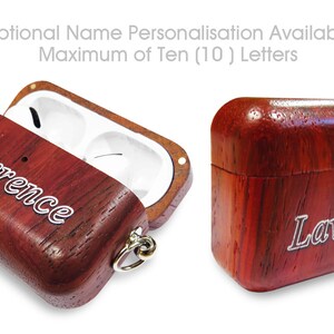 Puede incluir: Una funda de madera roja para AirPods con una inscripción plateada que dice "Lawrence". La funda está abierta para revelar el interior blanco y un pequeño gancho plateado.