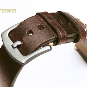 May include: Dark brown leather watch strap with a silver buckle and gold stitching.