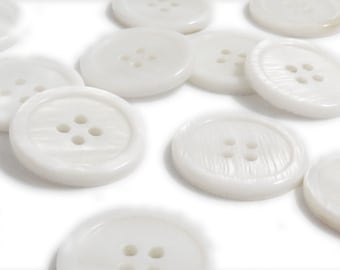 May include: A collection of white, round, four-hole buttons. The buttons are made of a smooth, shiny material and have a slightly raised edge.