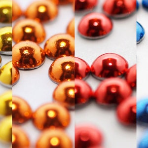 Può includere: Assortimento di decorazioni metalliche a forma di cupola nei colori oro, rame, rosso e blu. Le decorazioni sono disposte in file su una superficie bianca.
