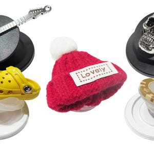 May include: Four different phone pop sockets with various designs. A red knitted hat with the word "Lovely" on it, a yellow and black pair of clogs, a silver guitar, and a silver skull.