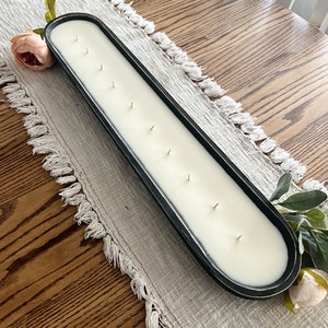 An above view of a black dough bowl candle with ten wicks sitting on a white table runner on a light brown table