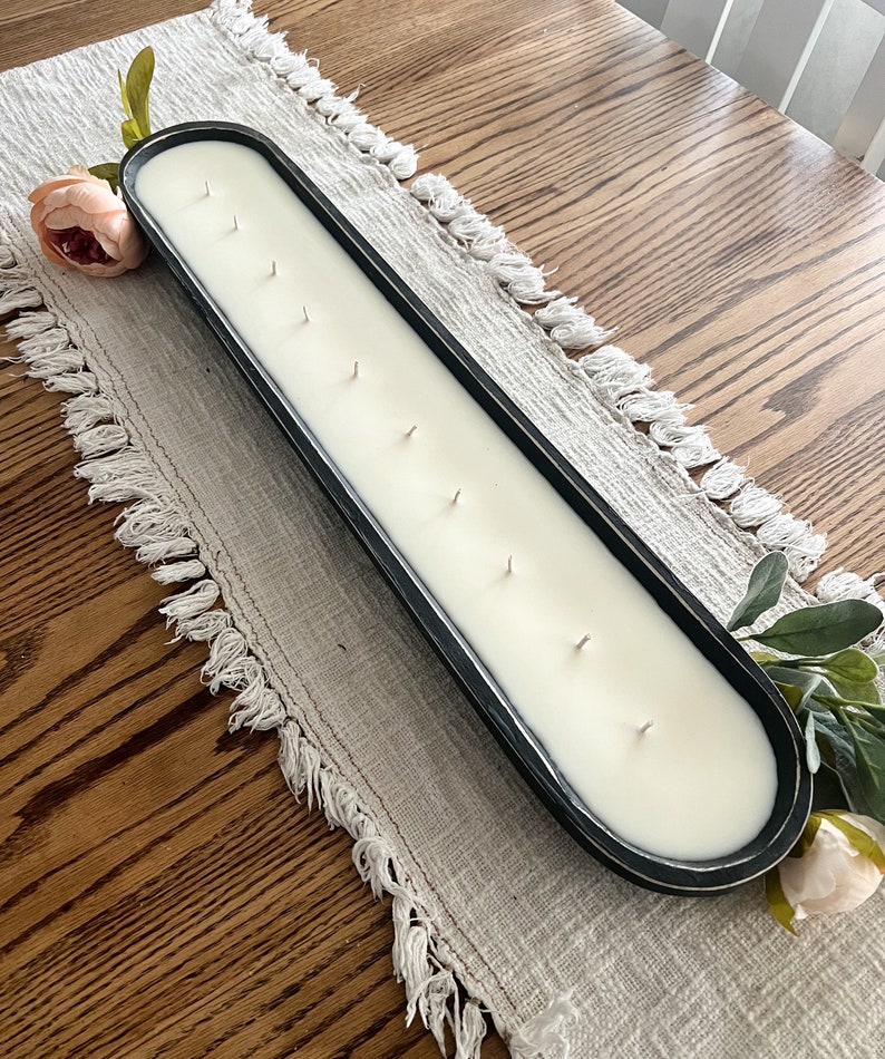 An above view of a black dough bowl candle with ten wicks sitting on a white table runner on a light brown table