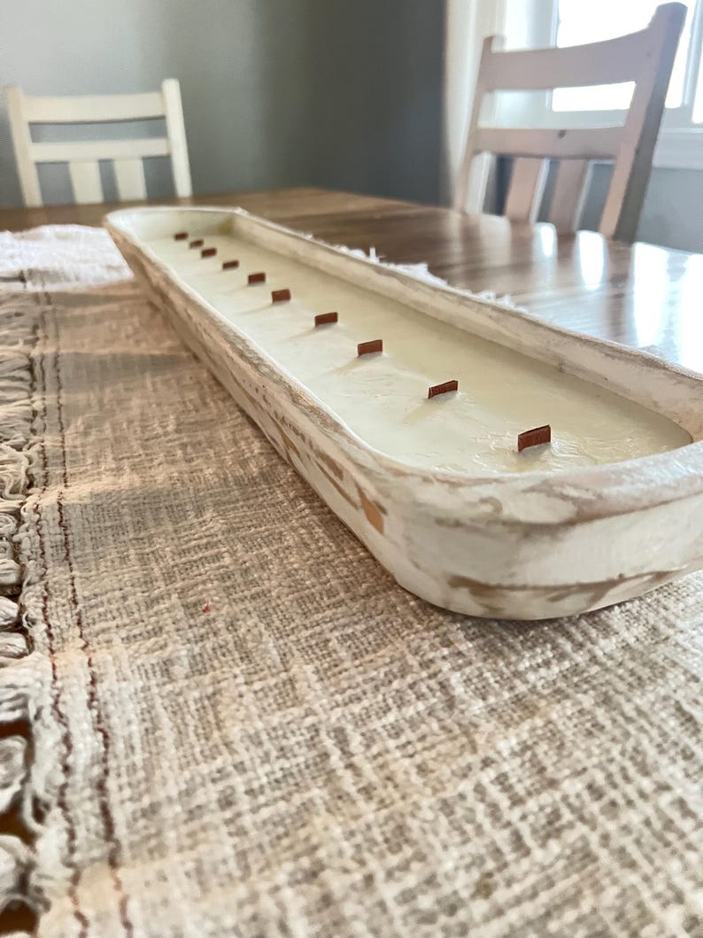 A white dough bowl candle unlit with wooden wicks sitting on a white table runner