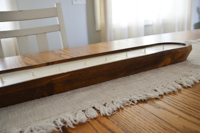 A side view of a brown dough bowl candle with cotton wicks unlit on a white table runner