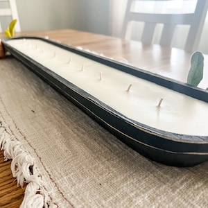 A close up of an unlit black dough bowl candle with cotton wicks on a white table runner