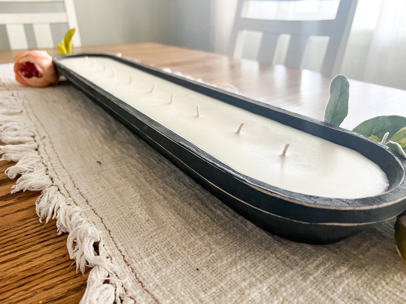A close up of an unlit black dough bowl candle with cotton wicks on a white table runner
