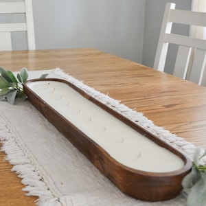 An unlit brown dough bowl candle with ten wicks sitting on a white table runner