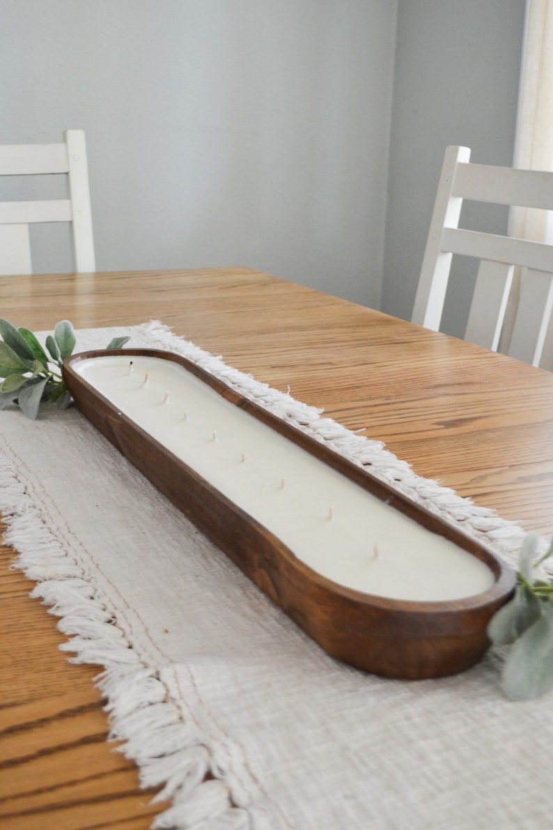 An unlit brown dough bowl candle with ten wicks sitting on a white table runner