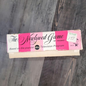 May include: Vintage "The Newlywed Game" box by Hasbro. The box features a pink and white striped design with the game title in elegant script. The box is based on the popular ABC Television Program.