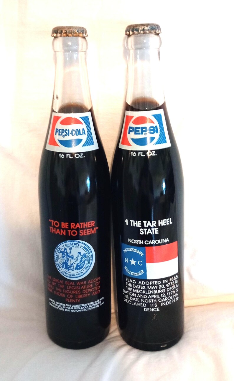May include: Two 16-ounce Pepsi-Cola bottles with commemorative labels. The left bottle features the Great Seal of the State of North Carolina with the text "To be rather than to seem". The right bottle features the North Carolina state flag with the text "1 The Tar Heel State" and a description of the flag's history.