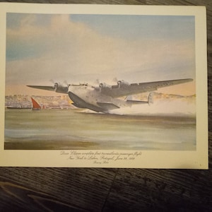 May include: A vintage illustration of a silver airplane taking off over a city skyline. The caption reads "Pine Clipper completes first transatlantic passenger flight, New York to Lisbon, Portugal, June 28, 1939".