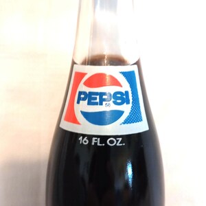 May include: A glass bottle of Pepsi-Cola with a blue and red logo and the text "Pepsi" and "16 FL. OZ."