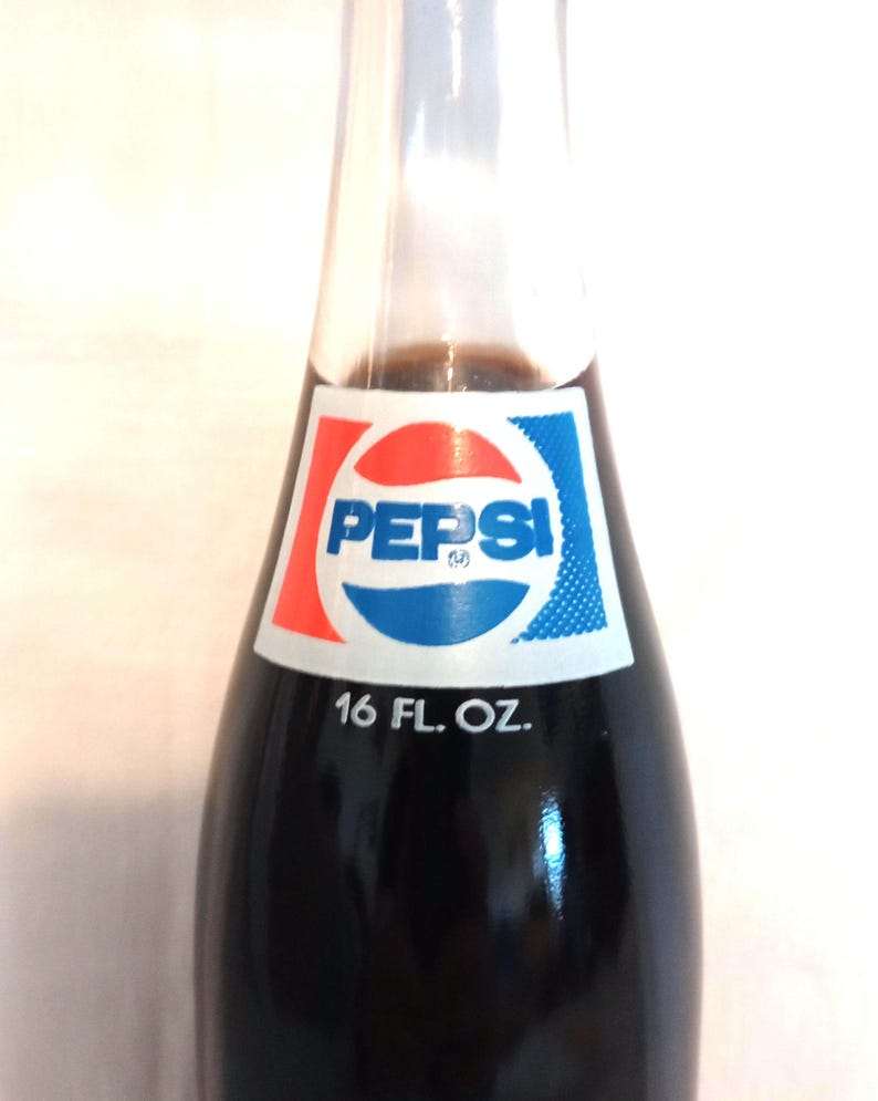 May include: A glass bottle of Pepsi-Cola with a blue and red logo and the text "Pepsi" and "16 FL. OZ."