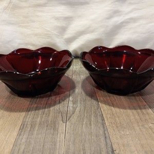 Peut inclure: Deux bols en verre rouge avec des bords festonnés. Les bols sont vides et posés sur une surface en bois.