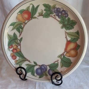 May include: A white ceramic plate with a green border and a fruit design. The design features peaches, grapes, cherries, plums, and pears.