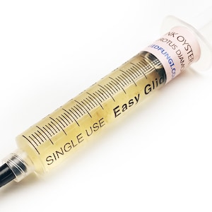 May include: A clear plastic syringe filled with a yellow liquid. The syringe is labelled "Single Use Easy Glide" and has a pink label that reads "Pink Oyster Pleurotus Djamor  Mycofungi.com".