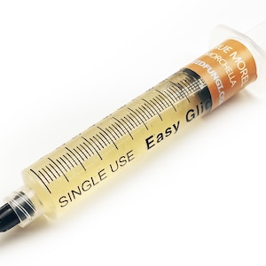 May include: A clear plastic syringe filled with a yellow liquid. The syringe is labelled "Single Use Easy Glic" and "True Morel Morchella Wildfungi.com".
