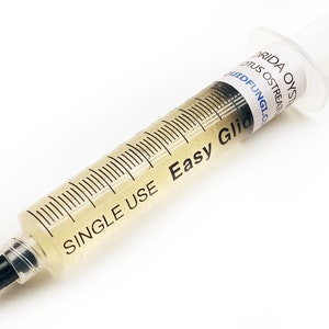 May include: A clear plastic syringe filled with a yellow liquid. The syringe is labelled "Single Use Easy Glic" and "Florida Oyster Lotus Oyster Treatment - MudFungi.com".