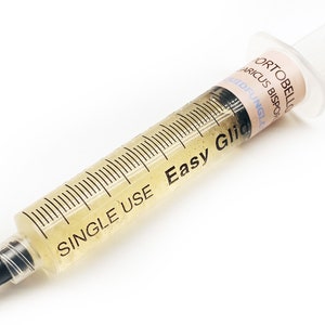 May include: A clear plastic syringe filled with a yellow liquid. The syringe is labelled "SINGLE USE Easy Glide".