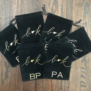 May include: Six black velvet drawstring bags with gold lettering. Each bag has the letters "b&k" with a heart in between. The bags also have the initials "BP" and "PA" printed on them.