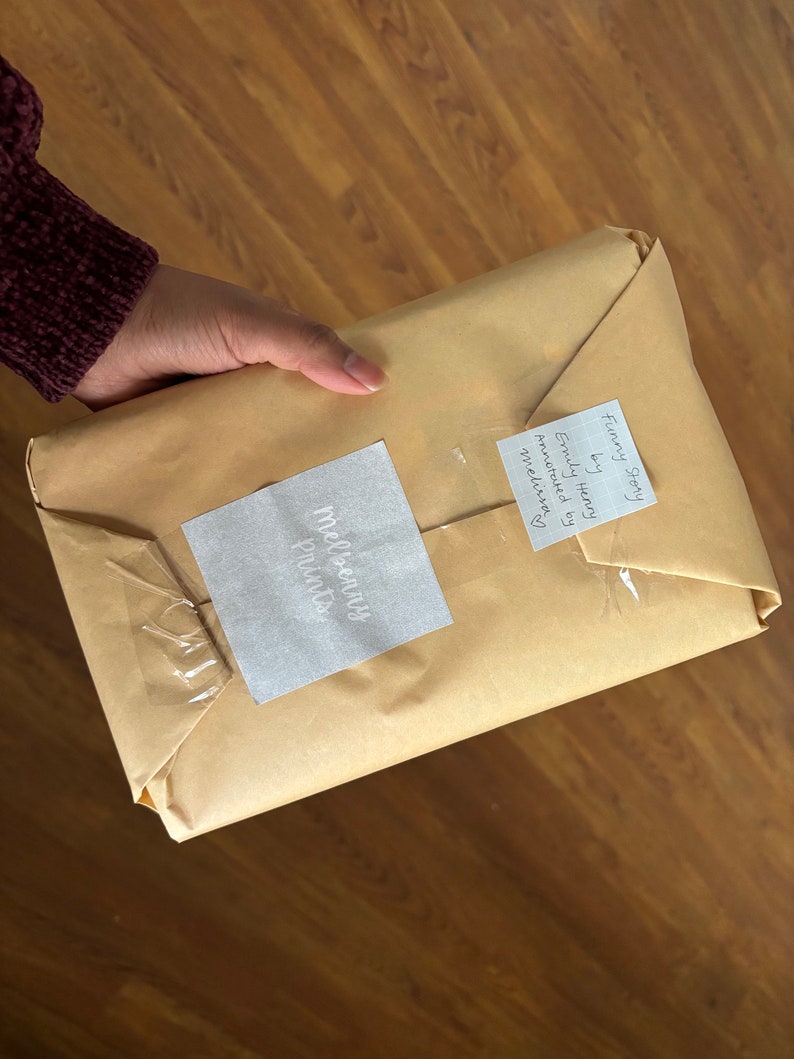 May include: A brown paper package with a white label that says "Melissany Prints" and a white sticky note that says "Funny Story by Emily Honey Annotated by Melissa"