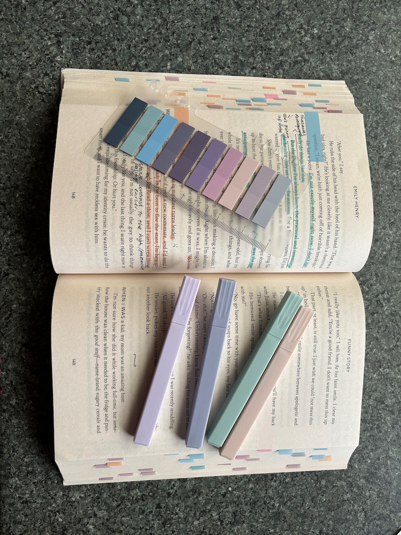 May include: A close-up of five pastel highlighters on a page of a book. The highlighters are in shades of lavender, light blue, and pink. The book is open to a page with text about a character named "Emily Henry".