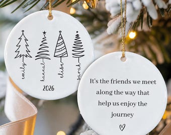 May include: Two round white ceramic ornaments with gold hanging strings. One ornament features four black line-art Christmas trees with the names Emily, Hannah, Elise, and Sarah, plus the year 2026. The other displays the text: It's the friends we meet along the way that help us enjoy the journey, with a small heart.