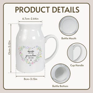 K&ouml;nnte beinhalten: Wei&szlig;er Keramikbecher mit gebogenem Henkel, mit dem Text "mom EST. 1999 grandma EST. 2026" in einem floralen Herzdesign. Der Becher ist 13 cm hoch und 8 cm breit. Die Produktdetails werden im Bild angezeigt.