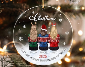 Può includere: Una decorazione natalizia rotonda e trasparente con tre figure viste di spalle che indossano maglioni festivi. Il testo recita Christmas, Evelyn, Phoebe, Rosie, 2026 e Our laughs, memories and friendships are endless. Include fiocchi.