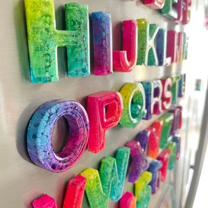 May include: A set of colorful alphabet magnets with a rainbow swirl design. Each letter is made of resin and has a magnetic backing.