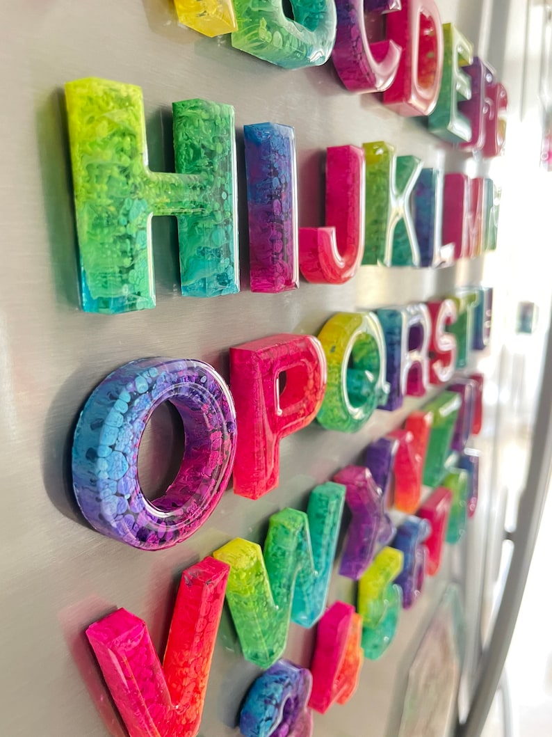 May include: A set of colorful alphabet magnets with a rainbow swirl design. Each letter is made of resin and has a magnetic backing.