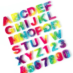 May include: Rainbow alphabet and number letter tiles made of resin with a speckled, glittery finish.