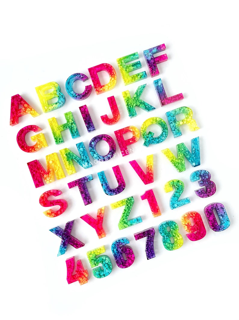 May include: Rainbow alphabet and number letter tiles made of resin with a speckled, glittery finish.